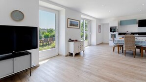 A modern kitchen with a dining area, large windows, and a flat-screen TV. - Ty Glas Guesthouse – Ground Floor Room (Pleubian)