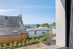 A residential area with a view of the sea, featuring houses with sloped roofs and a wooden fence in the foreground.