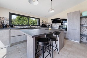 A modern kitchen with a large island, bar stools, a built-in oven, and a window overlooking greenery.