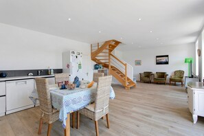 A modern kitchen with a dining area, a wooden staircase, and a living space with seating. - Ty Glas Guesthouse – Upstairs Room (Pleubian)