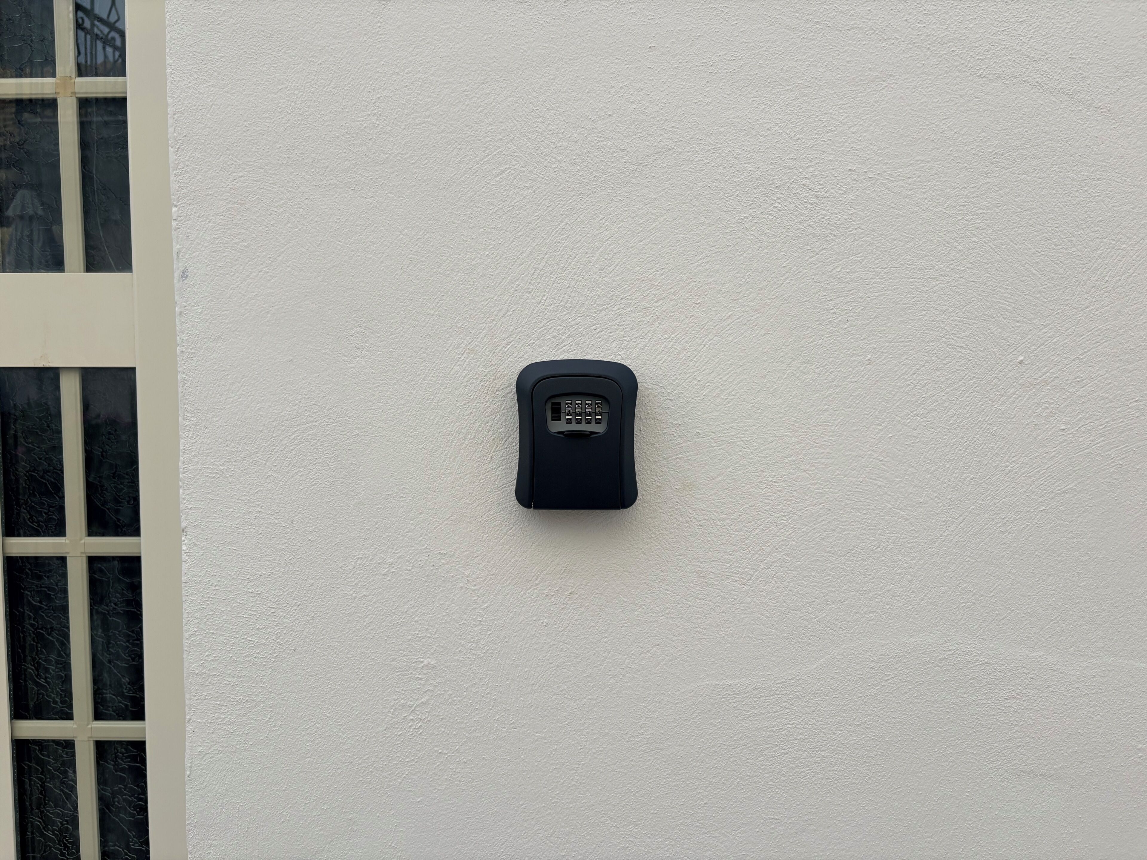 Um dispositivo de segurança fixado na parede, uma janela com moldura branca e uma parede texturizada.