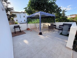 A patio with a covered seating area, a table, and a grill. - The Terrace (Villa San Leonardo)