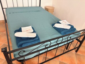 A bed with a teal bedspread, two folded towels, and a small round wooden stool beside it. - The Terrace (Villa San Leonardo)