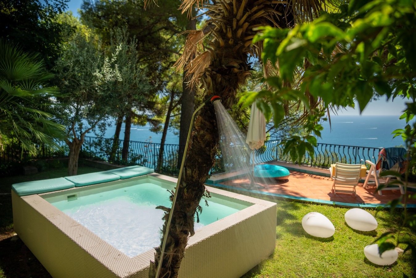 Une piscine avec vue sur la mer, entourée de verdure et agrémentée de mobilier d’extérieur.