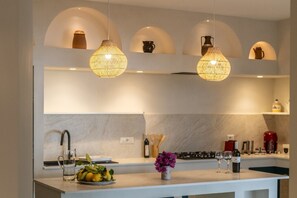 Una cucina moderna con luci a sospensione, una parete rivestita in marmo e un'isola centrale con una ciotola di frutta e bicchieri da vino.