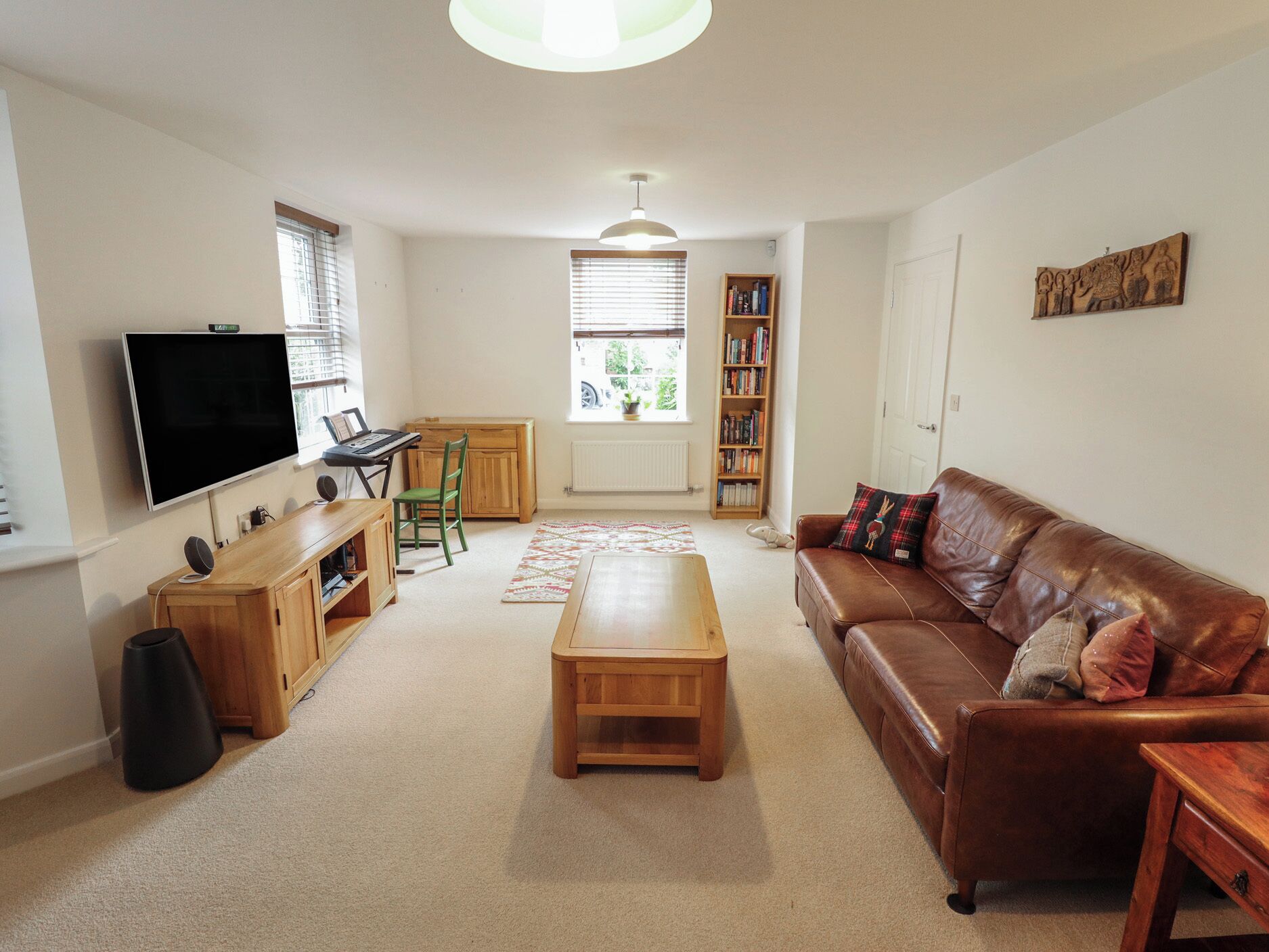 A living room with a television, a wooden desk, a green chair, a brown leather sofa, and a bookshelf.