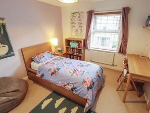 A bedroom with a bed, a bedside table with a lamp, a bookshelf, a window with curtains, and a radiator. - 26 Otho Way (Lincoln)