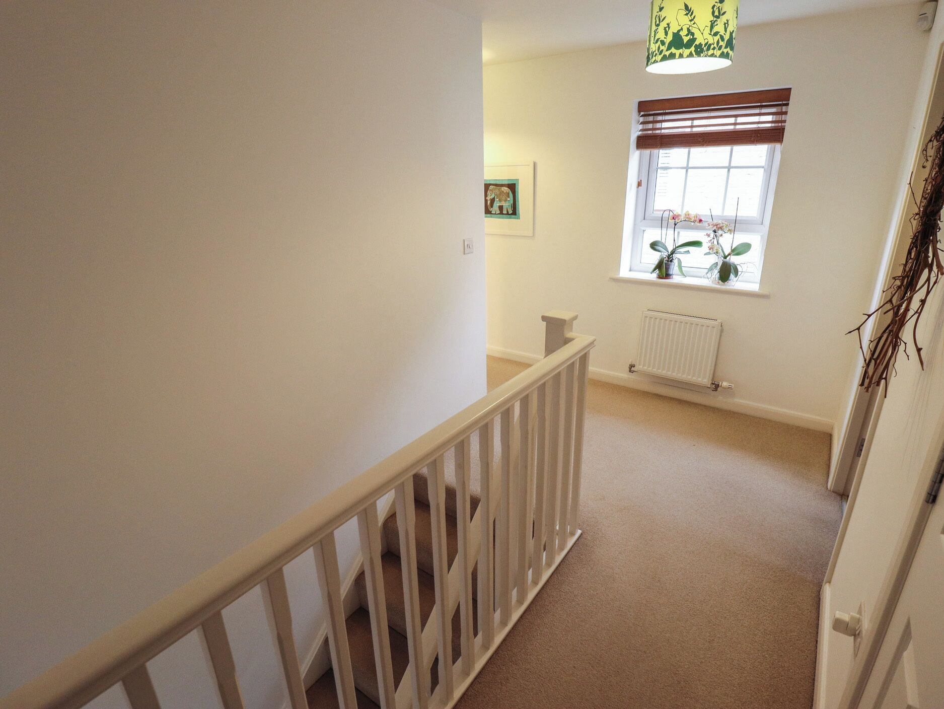 A narrow hallway with a white railing, a radiator, and a window with blinds.