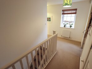 A narrow hallway with a white railing, a radiator, and a window with blinds.