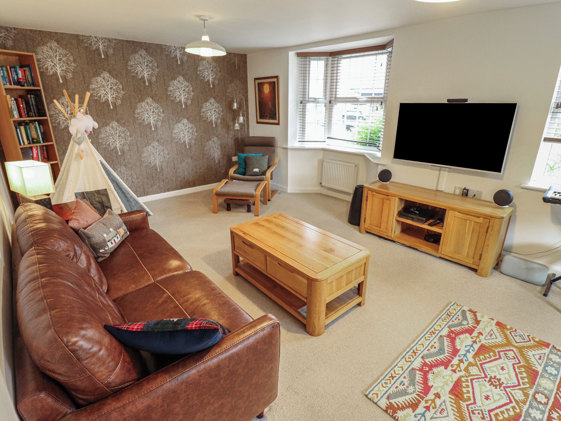 A living room with a brown leather sofa, a wooden coffee table, a bookshelf, a television, and a patterned rug.