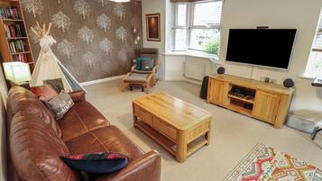 A living room with a brown leather sofa, a wooden coffee table, a bookshelf, a television, and a patterned rug.
