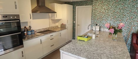A kitchen with white cabinets, a built-in oven, a range hood, a sink, and a countertop with a floral wallpaper pattern.