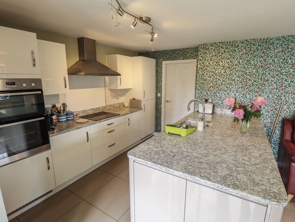 A kitchen with white cabinets, a built-in oven, a range hood, a sink, and a countertop with a floral wallpaper pattern. - 26 Otho Way (Lincoln)