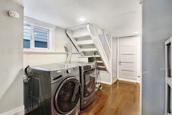 A laundry room with a washing machine and dryer, a staircase, and a door leading to another room. - The 23rd Ave Home (Seattle)