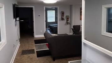 Een moderne woonkamer met een donkere bank, een glazen salontafel en een flatscreen televisie aan de muur.