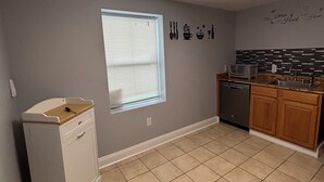 A kitchen with a dishwasher, a window with blinds, a wall with kitchen-themed decals, and a tiled floor. - 3-bedroom house in charming Clarksville with AC for relaxing stays (Clarksville)