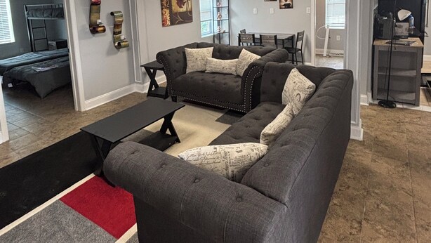 A living room with a sectional sofa, a coffee table, and a red rug. There is a dining area with a table and chairs in the background. - 3-bedroom house in charming Clarksville with AC for relaxing stays (Clarksville)