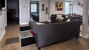 A living room with a large gray sofa, a dining area with a table and chairs, and a kitchen area with cabinets and a countertop. - 3-bedroom house in charming Clarksville with AC for relaxing stays (Clarksville)