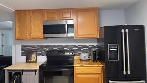 A kitchen with wooden cabinets, a microwave, a black refrigerator, a toaster, and a stove. - 3-bedroom house in charming Clarksville with AC for relaxing stays (Clarksville)