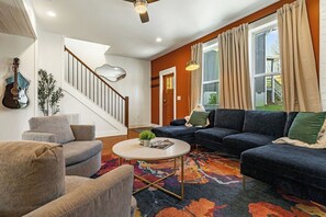 A living room with a staircase, a guitar, a sofa, and a coffee table. - Four Blue Ridge Houses with Hot Tubs (Asheville)