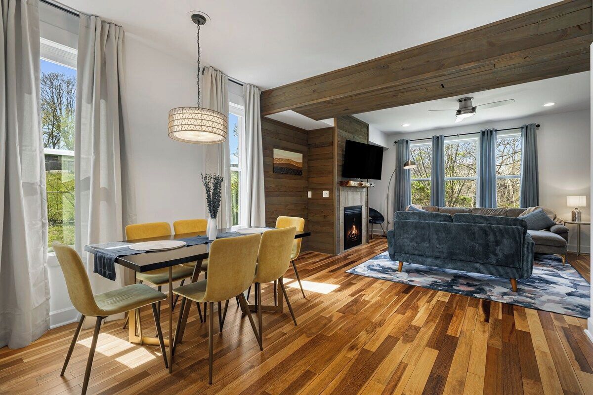Una sala de estar moderna con techo de madera, una chimenea, un sofá y un comedor con mesa y sillas.