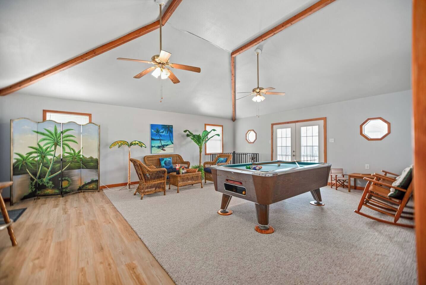 A spacious room with a pool table, wicker furniture, ceiling fans, and a large window.