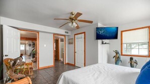 Ein Schlafzimmer mit einem Bett, einem Deckenventilator, einem Fernseher und einem Fenster mit Jalousien.