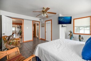 Ein Schlafzimmer mit einem Bett, einem Deckenventilator, einem Fernseher und einem Fenster mit Jalousien.