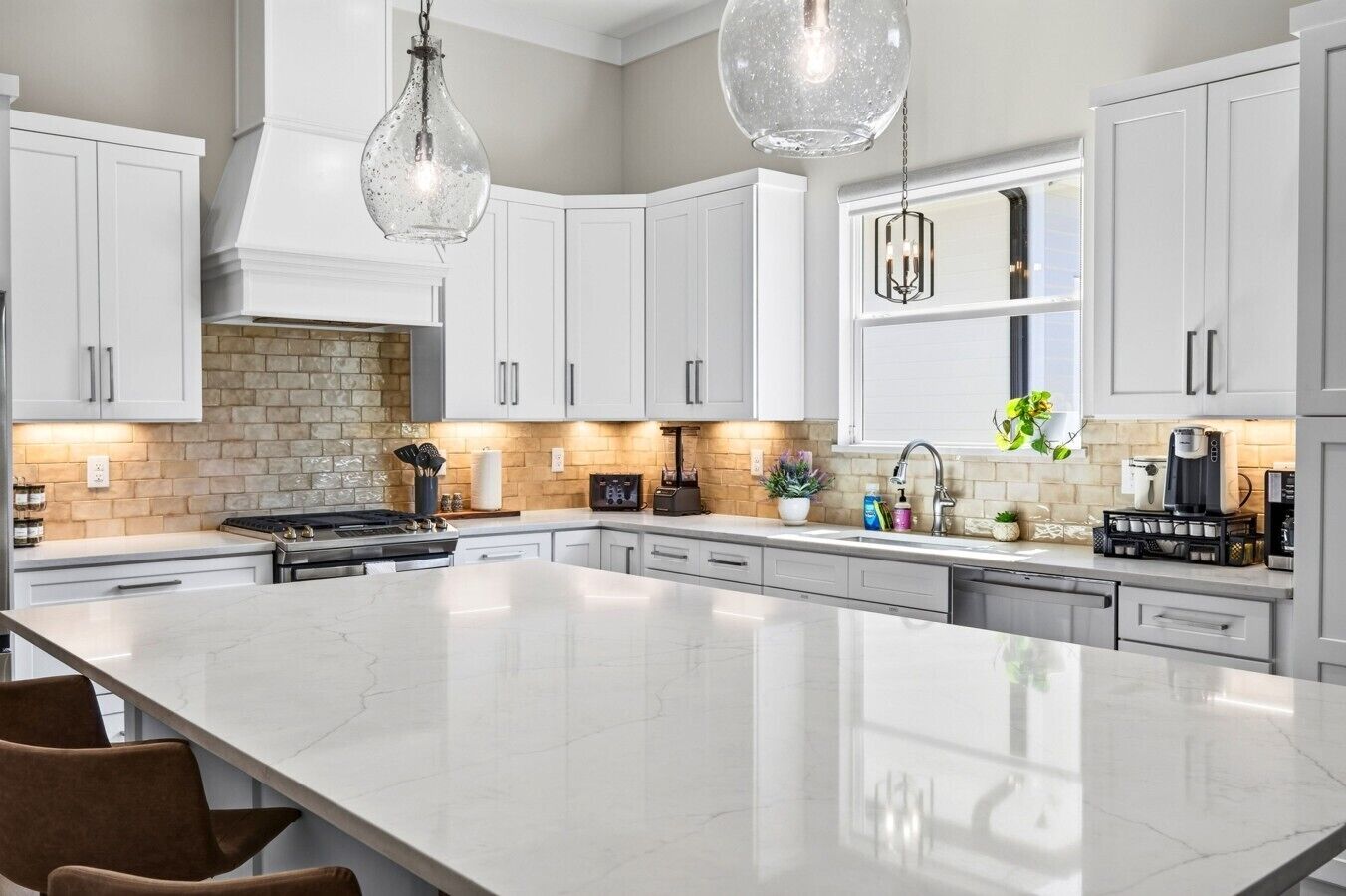 A modern kitchen with white cabinetry, a large island, and pendant lighting.