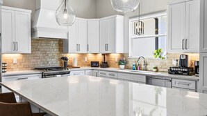 A modern kitchen with white cabinetry, a large island, and pendant lighting. - Caron House - Bay St. Louis (Bay St. Louis)