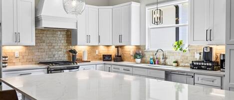 A modern kitchen with white cabinetry, a large island, and pendant lighting.
