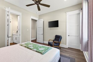 Ein Schlafzimmer mit Bett, Stuhl, Deckenventilator, Fernseher und einer Tür.