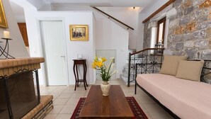 A living room with a fireplace, a sofa, a coffee table, and a staircase leading to an upper level. - Pleades Seaside Taygeta Gem in Mani, Near the Sea (Agios Nikolaos)