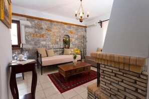 A living room with a stone wall, a sofa, a coffee table, and a fireplace. - Pleades Seaside Taygeta Gem in Mani, Near the Sea (Agios Nikolaos)