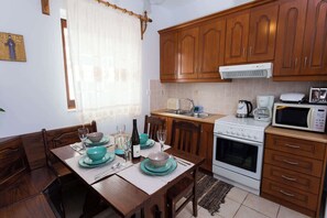 A kitchen with wooden cabinets, a stove, a microwave, and a dining table set with plates and glasses. - Pleades Seaside Asterope Gem in Mani, Near the Sea (Agios Nikolaos)