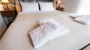 A neatly made bed with white linens and a folded towel with text, a headboard with a metal design, and bedside lamps on wooden nightstands. - Pleades Seaside Asterope Gem in Mani, Near the Sea (Agios Nikolaos)