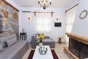 A living room with a stone wall, a fireplace, a sofa, a coffee table, and a television. - Pleades Seaside Asterope Gem in Mani, Near the Sea (Agios Nikolaos)