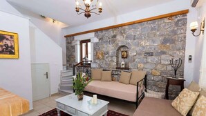A living room with a stone wall, a sofa, a coffee table, and a staircase. - Pleades Seaside Alcyone Gem in Mani, Near the Sea (Agios Nikolaos)