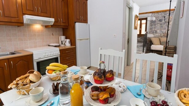 A kitchen with wooden cabinets, a white stove, and a dining table set with food and drinks. - Pleades Seaside Alcyone Gem in Mani, Near the Sea (Agios Nikolaos)