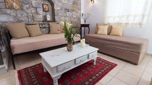 A living room with a stone wall, two sofas, a white coffee table, and a red patterned rug. - Pleades Seaside Alcyone Gem in Mani, Near the Sea (Agios Nikolaos)