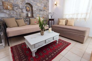 Ein Wohnzimmer mit Steinwand, zwei Sofas, einem weißen Couchtisch und einem roten Teppich mit Muster.