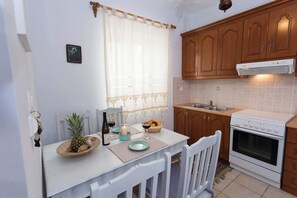 A kitchen with wooden cabinets, a white stove, a sink, and a dining area with a table set for two. - Pleades Seaside Alcyone Gem in Mani, Near the Sea (Agios Nikolaos)