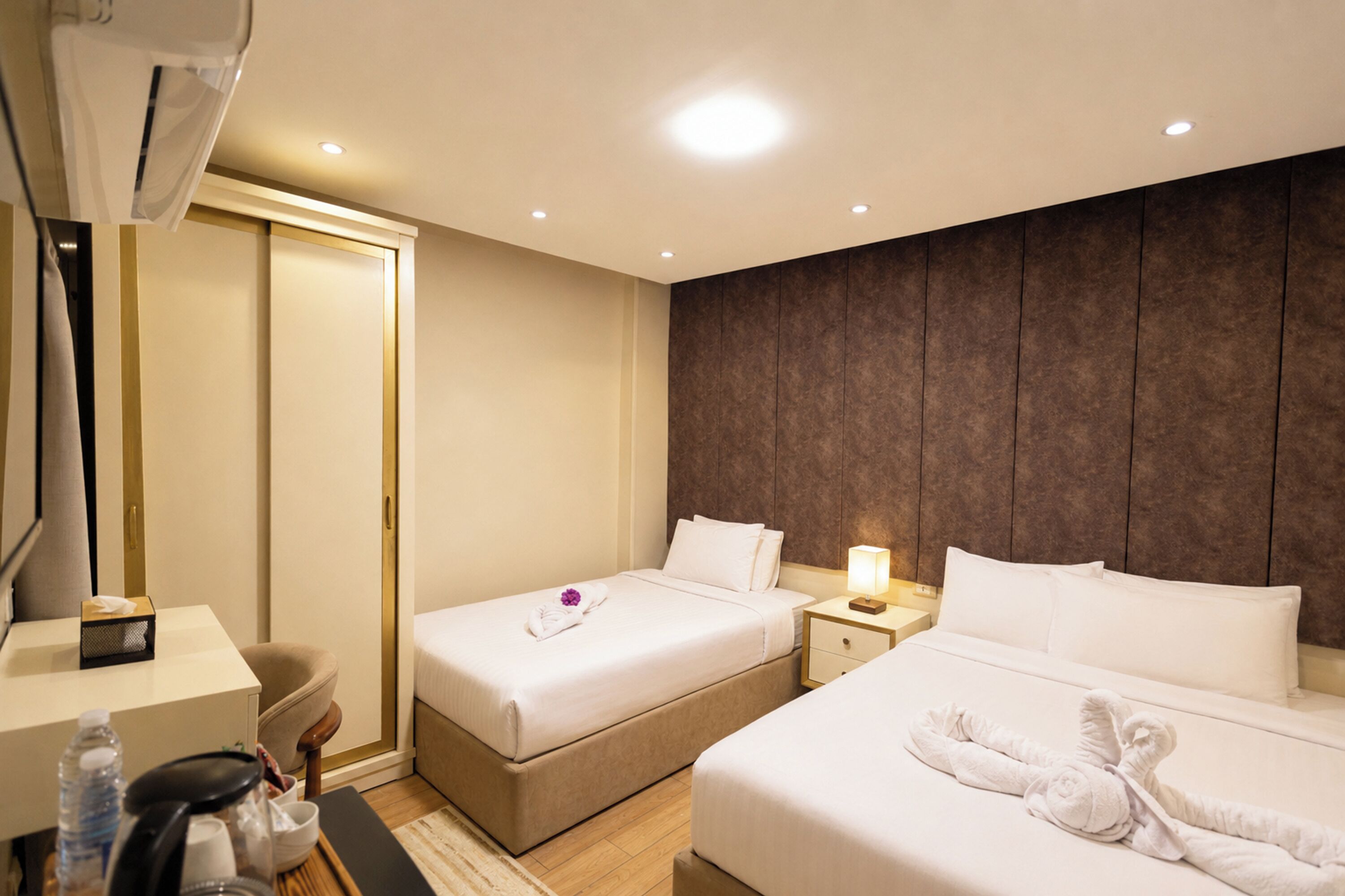 A hotel room with two beds, a desk, a chair, a bedside table with a lamp, and a wardrobe.