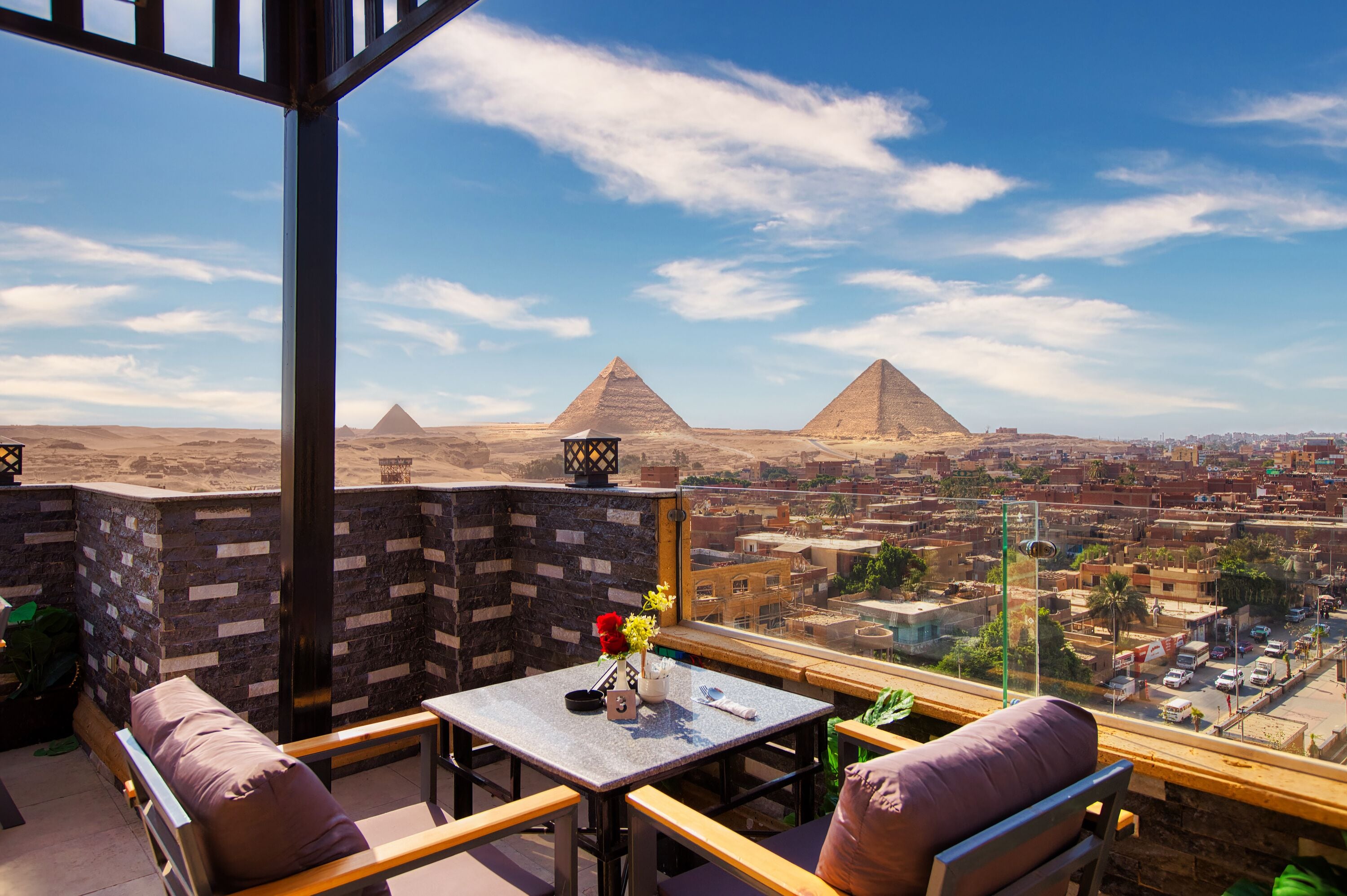 Una terraza con mesa y sillas, con vistas a un paisaje urbano y pirámides.