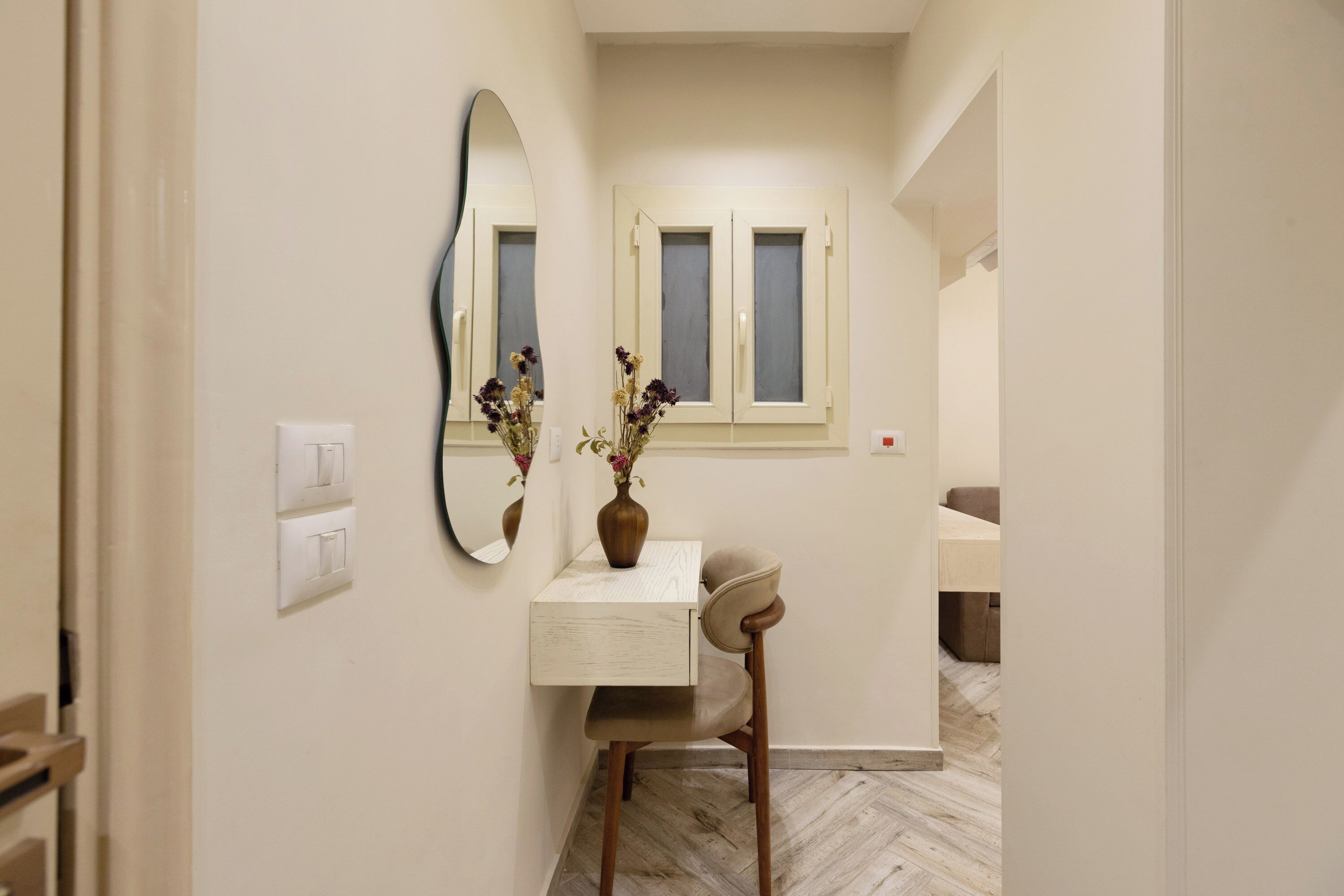 Un couloir étroit avec une coiffeuse, un miroir et une fenêtre dont les volets sont fermés.