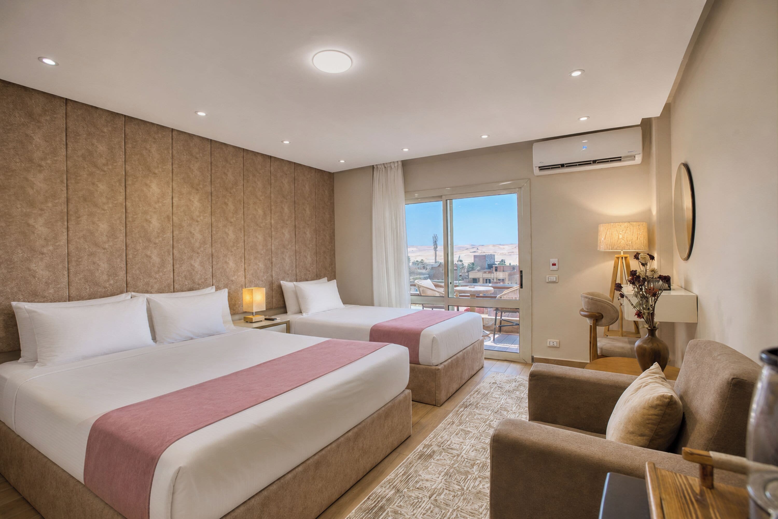 A hotel room with two beds, a sofa, a table, and a view of the city.