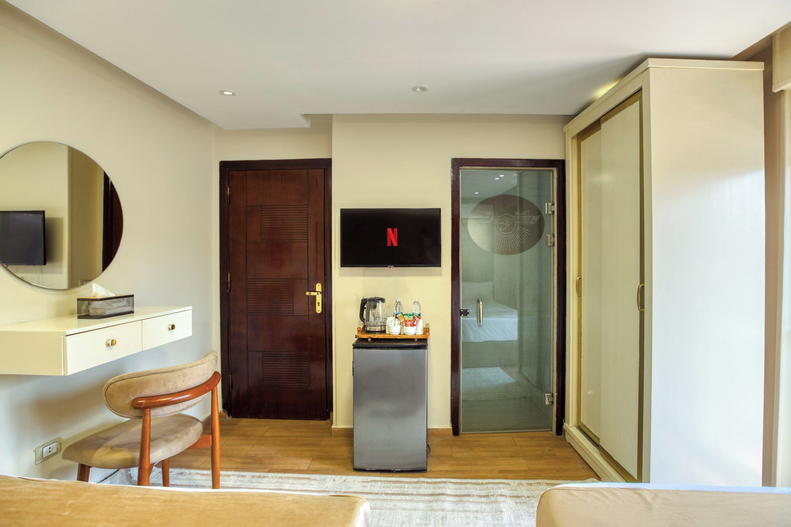 A hotel room with a bed, a desk with a chair, a TV, a minibar, and a wardrobe.