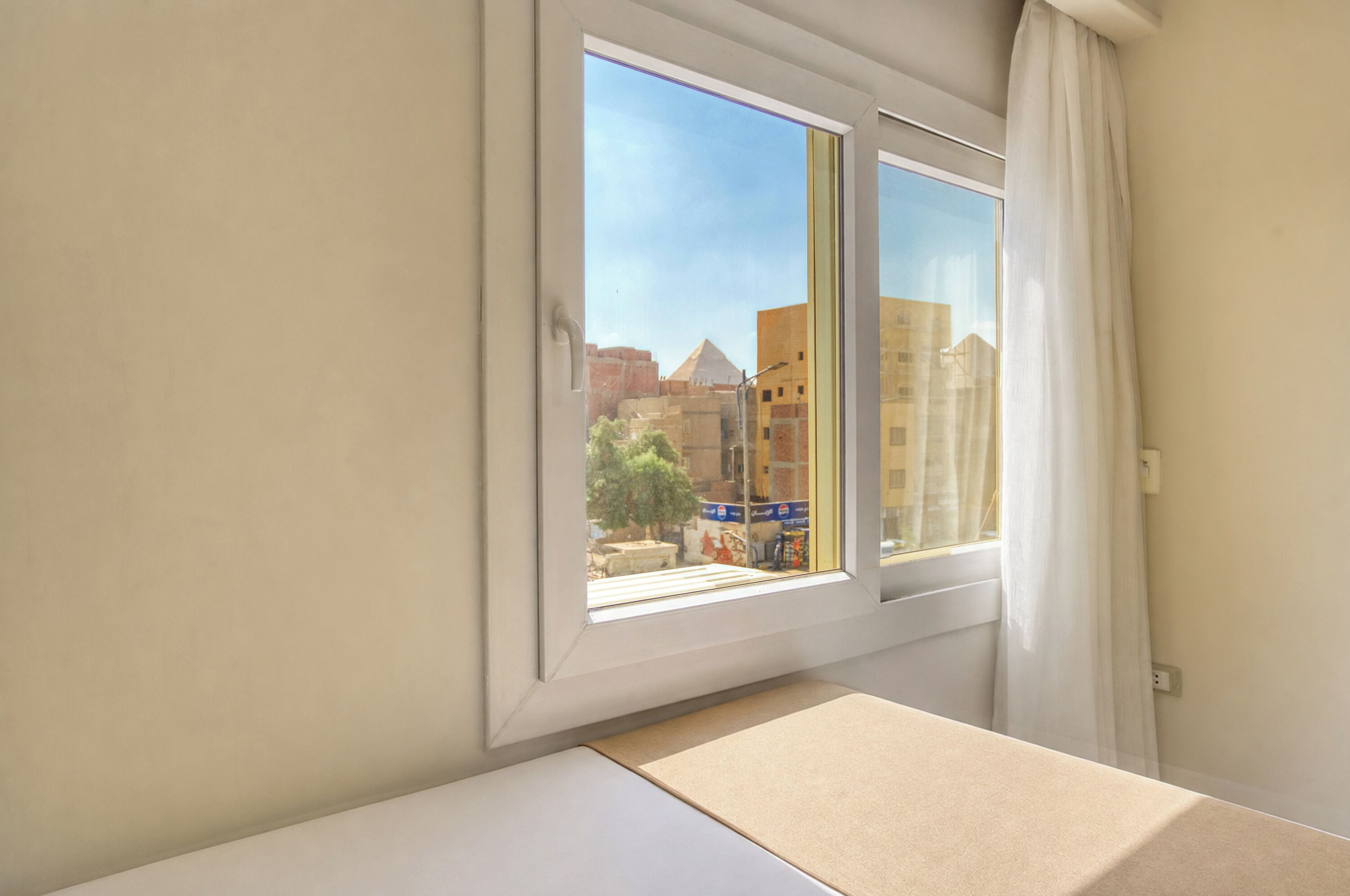 A room with a window overlooking a cityscape, a bed, and a white wall.