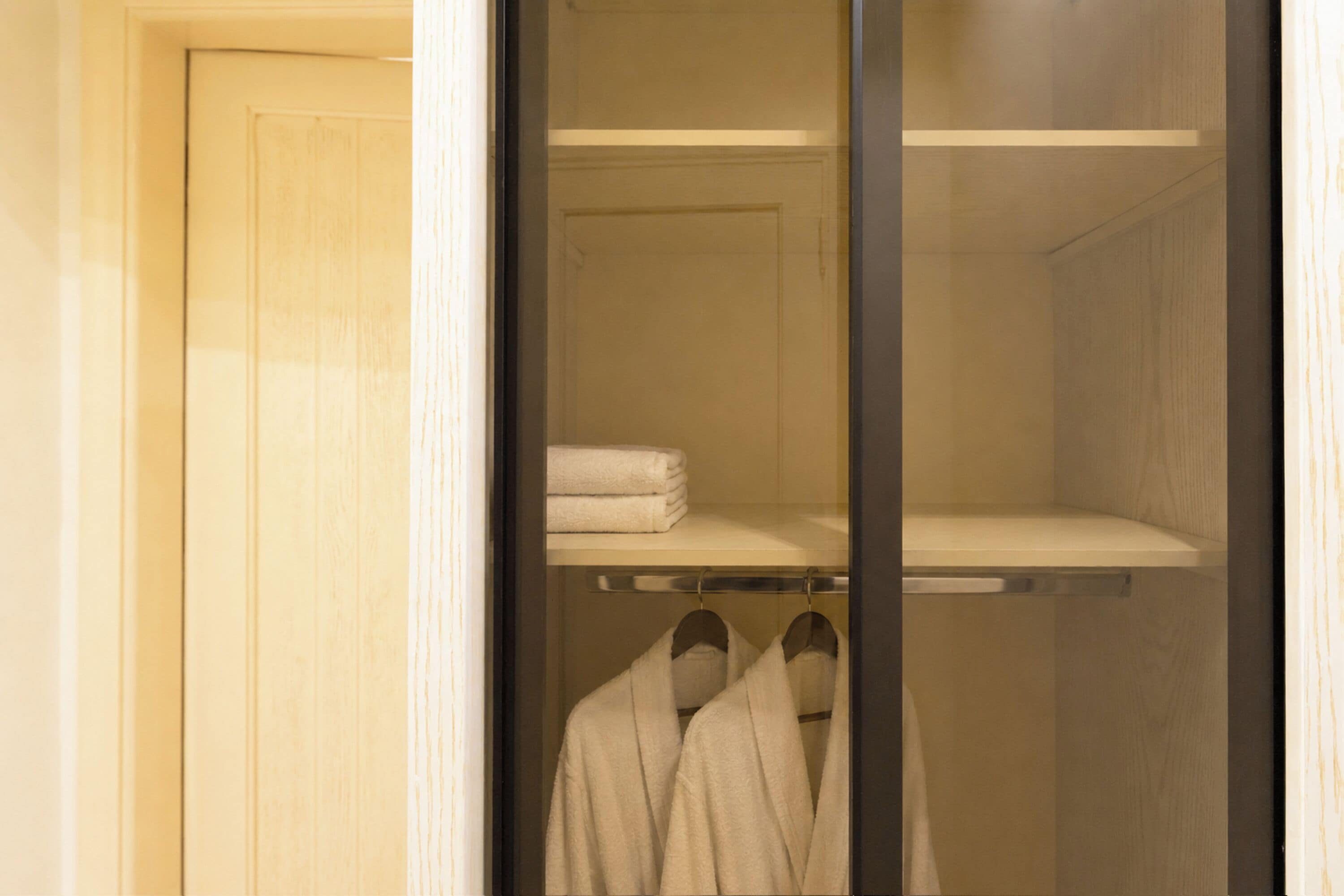 A walk-in closet with a mirrored door, a shelf with folded towels, and a rack with hanging robes.