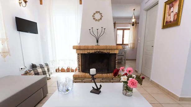 Een woonkamer met een open haard, een bank, een salontafel met decoratieve objecten, en een aan de muur bevestigde televisie.